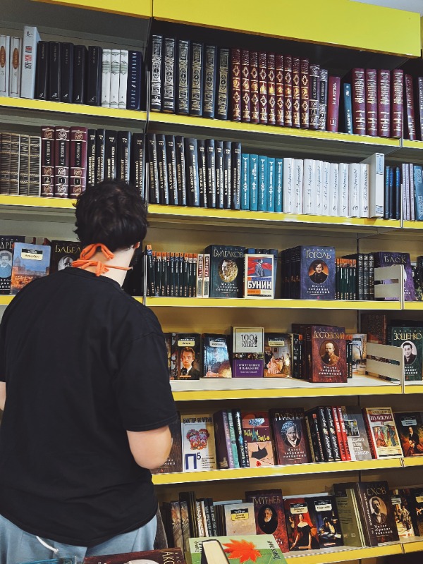 Interno di una libreria specializzata in testi russi. Ragazzo di spalle che indossa una maglietta nera e guarda i libri esposti